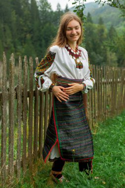 Bir buket kır çiçeğiyle gevşek saçlı kız tahta bir çitin önünde duruyor.