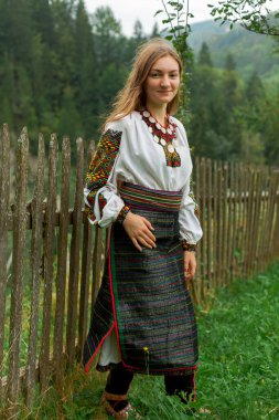 Bir buket kır çiçeğiyle gevşek saçlı kız tahta bir çitin önünde duruyor.