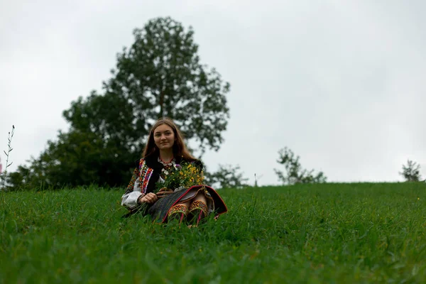 野生の花の花束で刺繍の女の子は緑の草の中に座っている — ストック写真