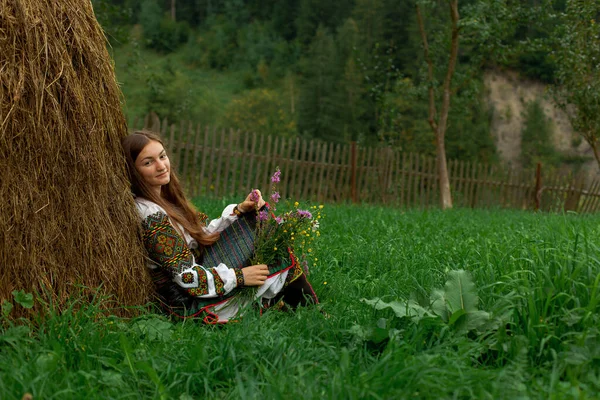 野の花の花束を持つ緩やかな髪の女の子は彼女と一緒に座っています彼女の背中に干し草 — ストック写真