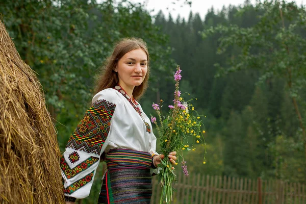 Bir buket kır çiçeğiyle dağınık saçlı kız samanlığın yanında duruyor.