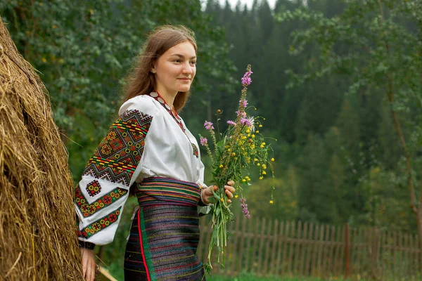 Bir buket kır çiçeğiyle dağınık saçlı kız samanlığın yanında duruyor.