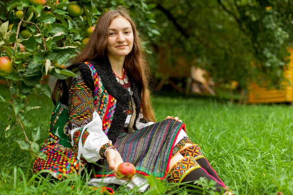 一个戴着绣花的成熟苹果的女孩坐在一棵苹果树下的绿草上 — 图库照片