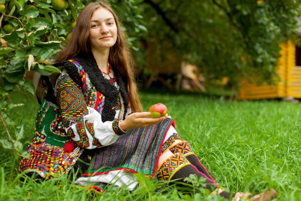 一个戴着绣花的成熟苹果的女孩坐在一棵苹果树下的绿草上 — 图库照片