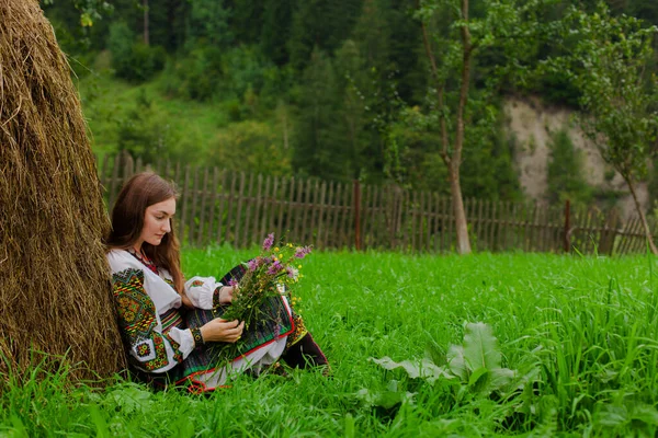 野の花の花束を持つ緩やかな髪の女の子は彼女と一緒に座っています彼女の背中に干し草 — ストック写真