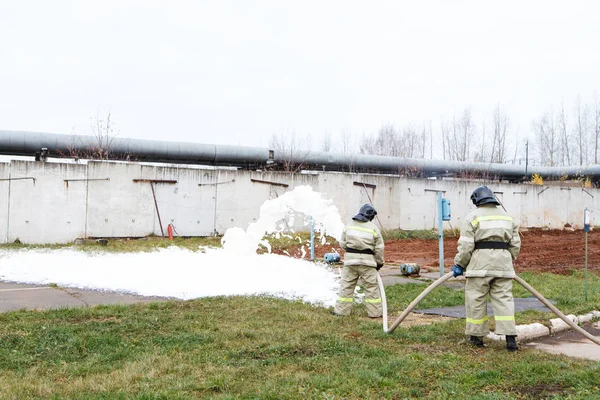 Firefighters extinguish the fire with a chemical foam coming from the fire engine through a long hose