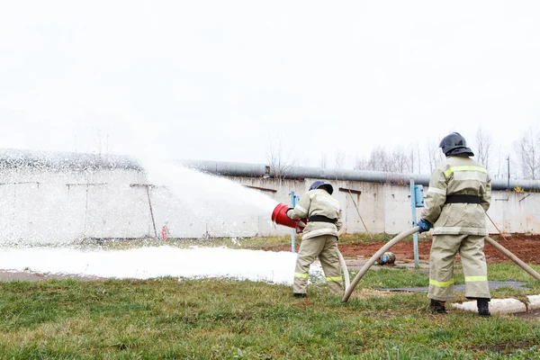 Firefighters extinguish the fire with a chemical foam coming from the fire engine through a long hose
