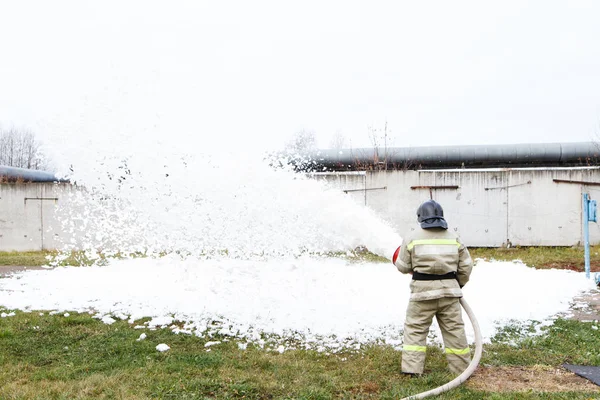 Firefighters extinguish the fire with a chemical foam coming from the fire engine through a long hose