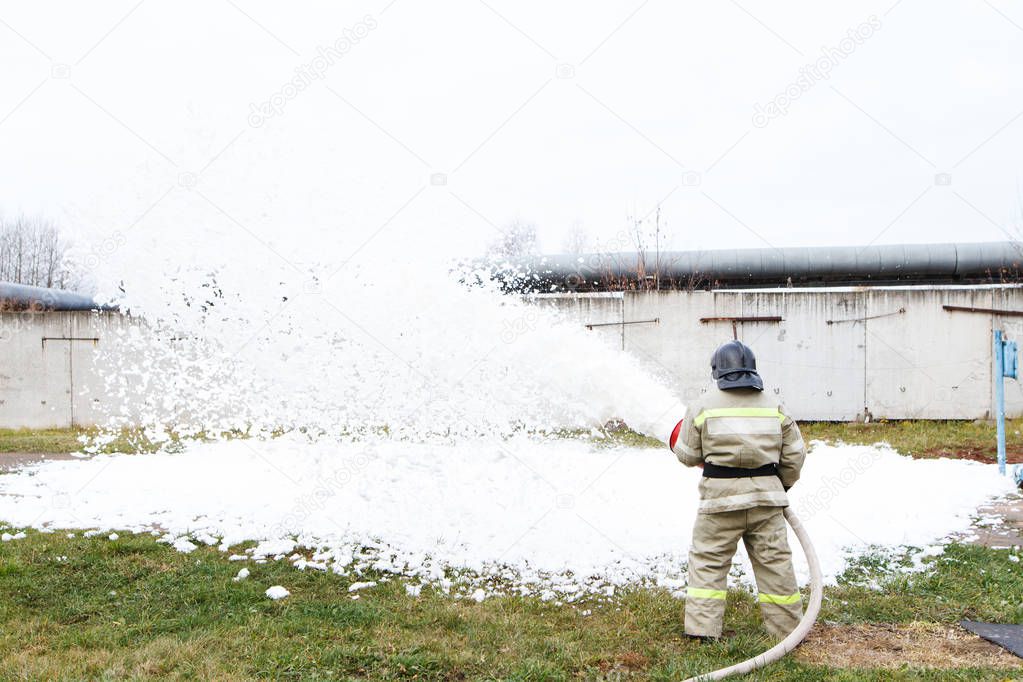 Firefighters extinguish the fire with a chemical foam coming from the fire engine through a long hose