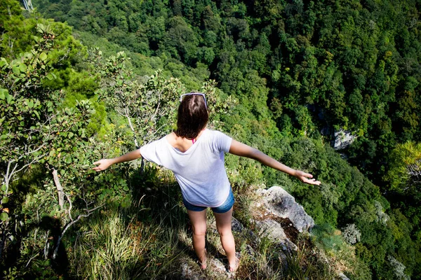 A girl stands on the edge of a mountain cliff spreading her arms — Stock Photo, Image