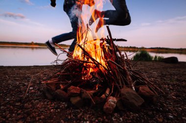 Bir adam ve bir kız yanan ateşin üzerinde arka plan atlamak