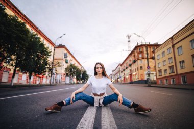 Sokak kentsel tarzı. Örgü gömlek ve kot kız. Kız yol ortasında oturan poz.
