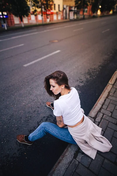 La chica se sienta al borde de la carretera. Calle estilo urbano . — Foto de Stock