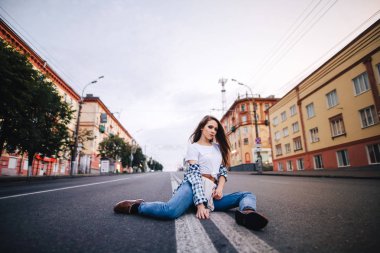 Örgü gömlek ve kot kız. Kız yol ortasında oturan poz.