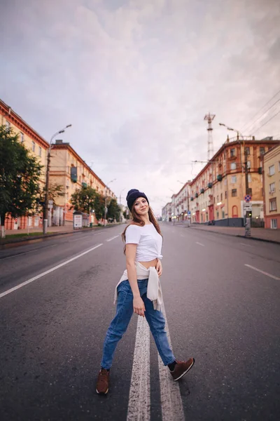 Chica posando en medio de la carretera. Chica con ropa elegante y sombrero . — Foto de Stock