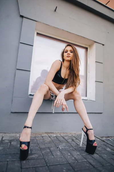 Chica en tacones altos posando entre las calles de la ciudad. Chica en un top negro y pantalones cortos . — Foto de Stock