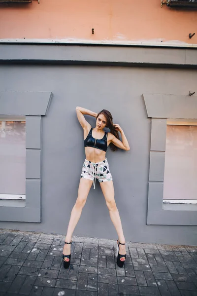 Flicka i höga klackar poserar bland gatorna i staden. Flicka i en svart topp och korta shorts. — Stockfoto