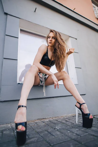 Chica en tacones altos posando entre las calles de la ciudad. Chica en un top negro y pantalones cortos . Imágenes de stock libres de derechos