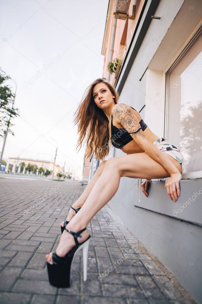 Girl in high heels posing among the streets of the city. Girl in a black top and short shorts.
