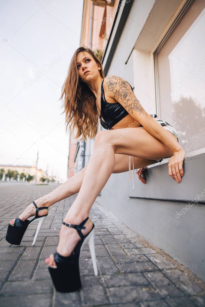 Girl in high heels posing among the streets of the city. Girl in a black top and short shorts.