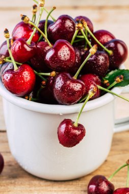 Kiraz ahşap bir masa, taze kiraz, mevsim meyveleri, tatlı çilek, kiraz, Olgun bir beyaz emaye kupa için tanıtıcı içinde çilek