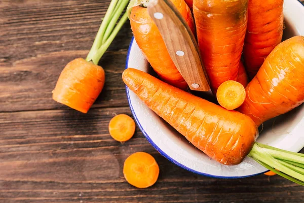 carrots in white enamel plate, wooden background, fresh vegetables