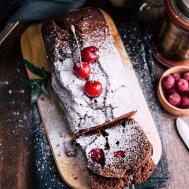 Kiraz koyu ahşap arka plan üzerinde pudra şekeri toz, fincan kahve, tatlı, fırın ürünleri ile çikolatalı pasta