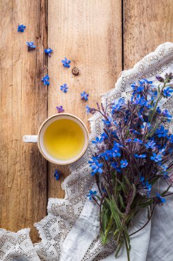 mavi çiçek, bir fincan çay ve bir beyaz dantel masa örtüsü ahşap bir masa üzerinde bir buket