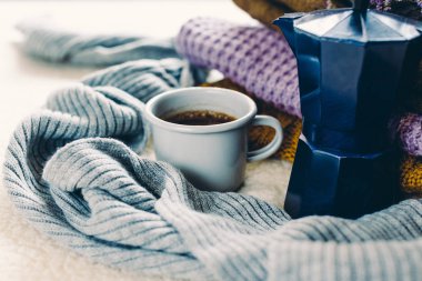 Kupa ve mavi kahve şofben cezve beyaz yorgan, örme elbise yığını ve bir eşarp