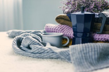 Kupa ve mavi kahve şofben cezve beyaz yorgan, örme elbise yığını ve bir eşarp