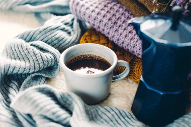 Kupa ve mavi kahve şofben cezve beyaz yorgan, örme elbise yığını ve bir eşarp