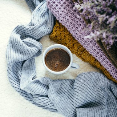 Bir kupa kahve beyaz bir battaniye ve bir örme elbise yığını