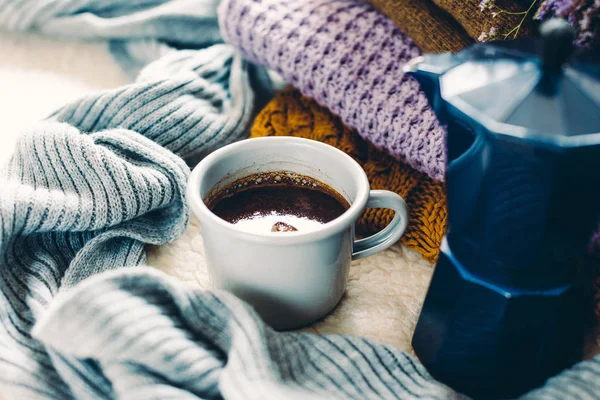 Kupa ve mavi kahve şofben cezve beyaz yorgan, örme elbise yığını ve bir eşarp