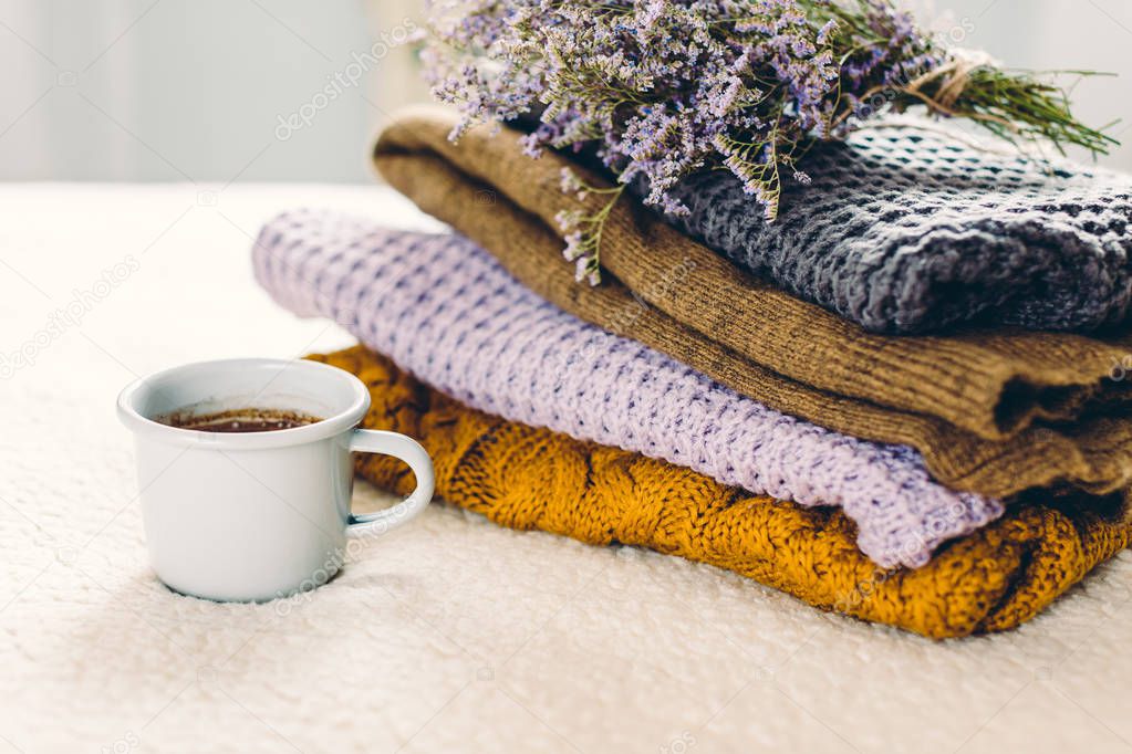 A mug of coffee on a white blanket and a pile of knitted clothes