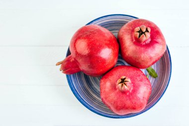 Beyaz ahşap zemin üzerinde mavi bir tabak içinde nar