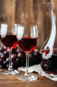 Červené víno, karafa, dvě skleničky a tmavými hrozny na dřevěné pozadí