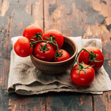 Bir dal, kil kase, keten peçete ve ahşap arka plan, taze sebze olgun domates