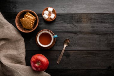 Çay, elma, kurabiye ve şeker bir siyah ahşap masa, Kahvaltı, snack, üstten görünüm
