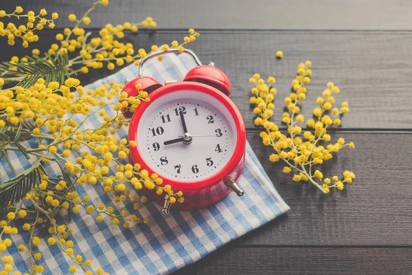 赤い目覚まし時計 黒の木製の背景 ミモザ 黄色の花 — ストック写真