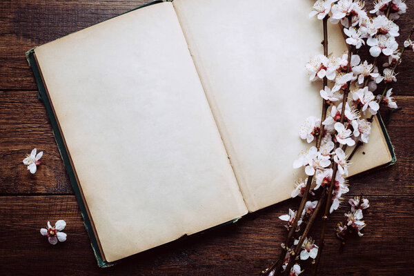 Retro background, old book and blossoming cherry branches on a wooden table
