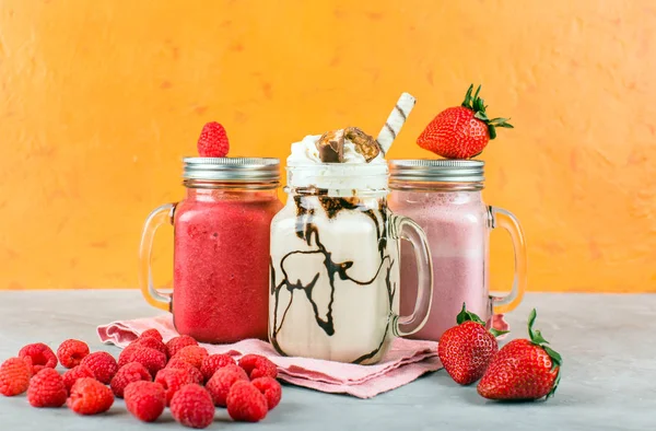 Various non-alcoholic cocktails, raspberry and strawberry smoothies, bright orange background