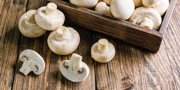 Fresh champignons in a box on a wooden background, long banner