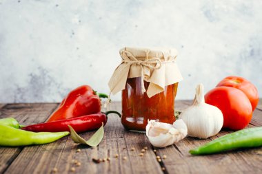 Ahşap bir arka plan üzerinde bir kavanozda Adjika, baharatlı domates sosu