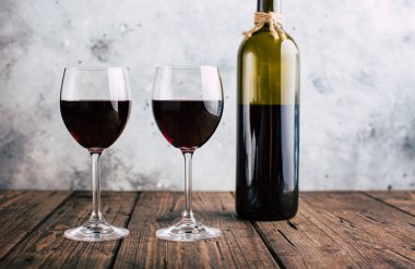 İki bardak kırmızı şarap ve bir şişe, gri sıva arka plan