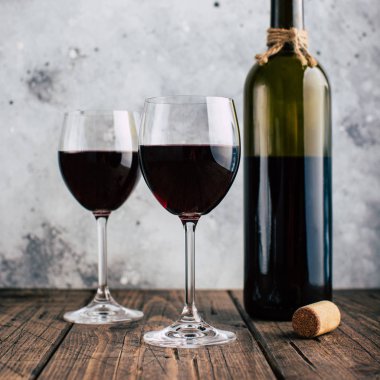 İki bardak kırmızı şarap ve bir şişe, gri sıva arka plan