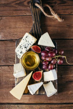 Ahşap kesme tahtası üzerinde çeşitli peynir, bal, üzüm ve incir