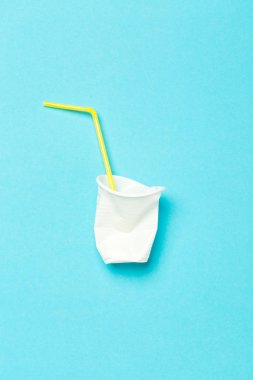 Beyaz plastik bardak ve sarı pipet mavi arka planda kokteyl için.