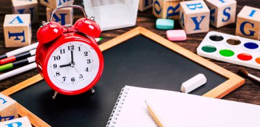 Okula dönüş kavramı. Alarm saati, tebeşir, kalem, defter, kırtasiye malzemesi, tebeşir tahtası arkaplanı. Tasarım. Boşluğu Kopyala 