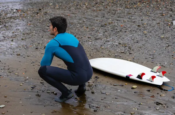 Surfer Crouches Thoughtfully Rocky Beach Next His Surfboard Contemplating Ocean — Stock Photo, Image
