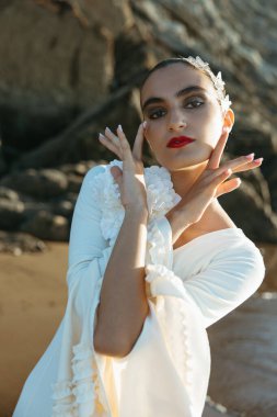 Young brunette dancer poses with hands by the shore at golden hour